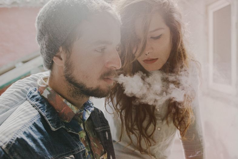 A couple shares an intimate moment in soft lighting with vapor or smoke visible.