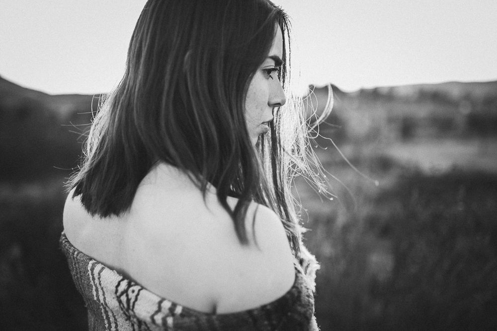A black and white side profile portrait with wind-blown hair against a natural landscape.