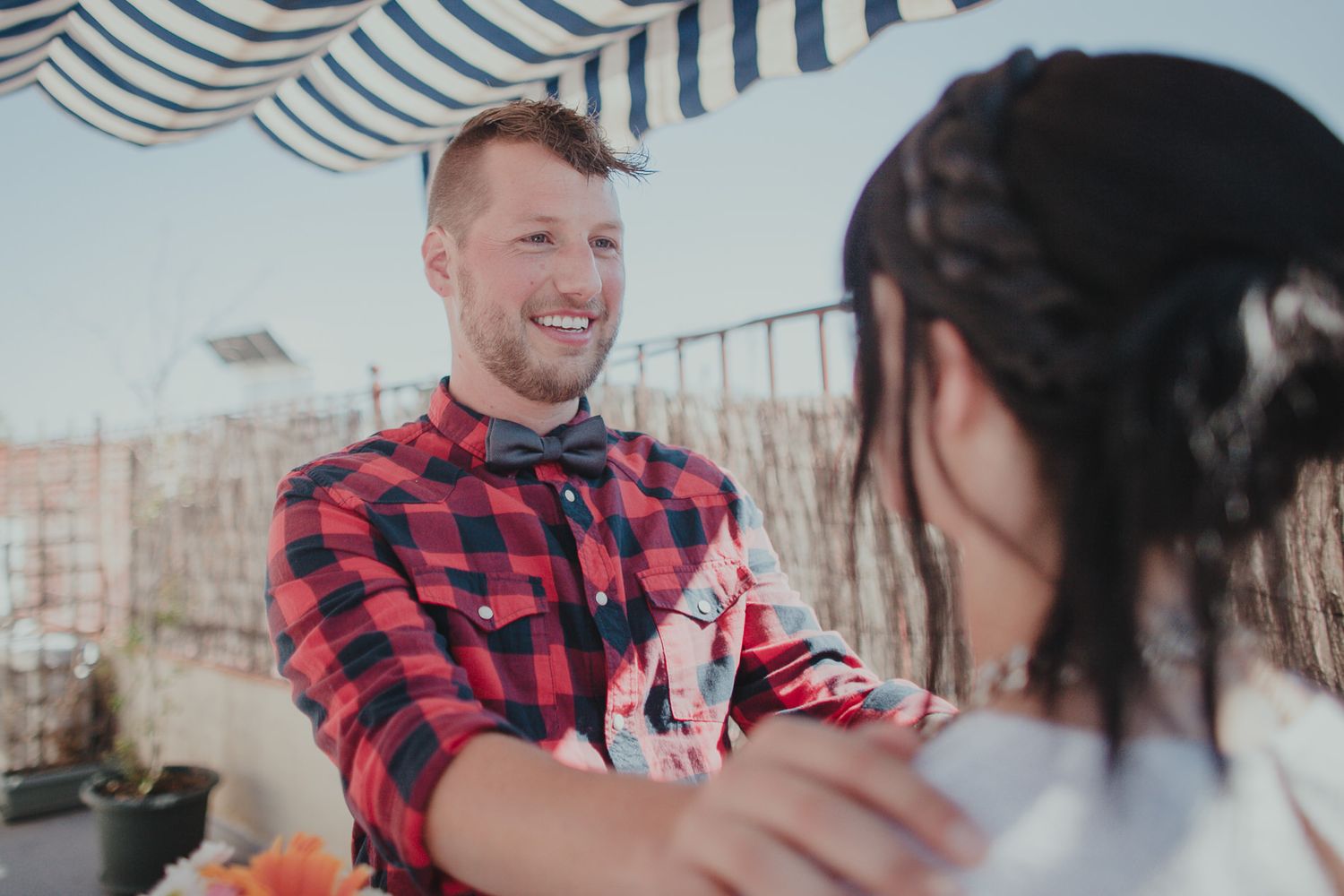 Two people interacting on a rooftop terrace under striped awning.