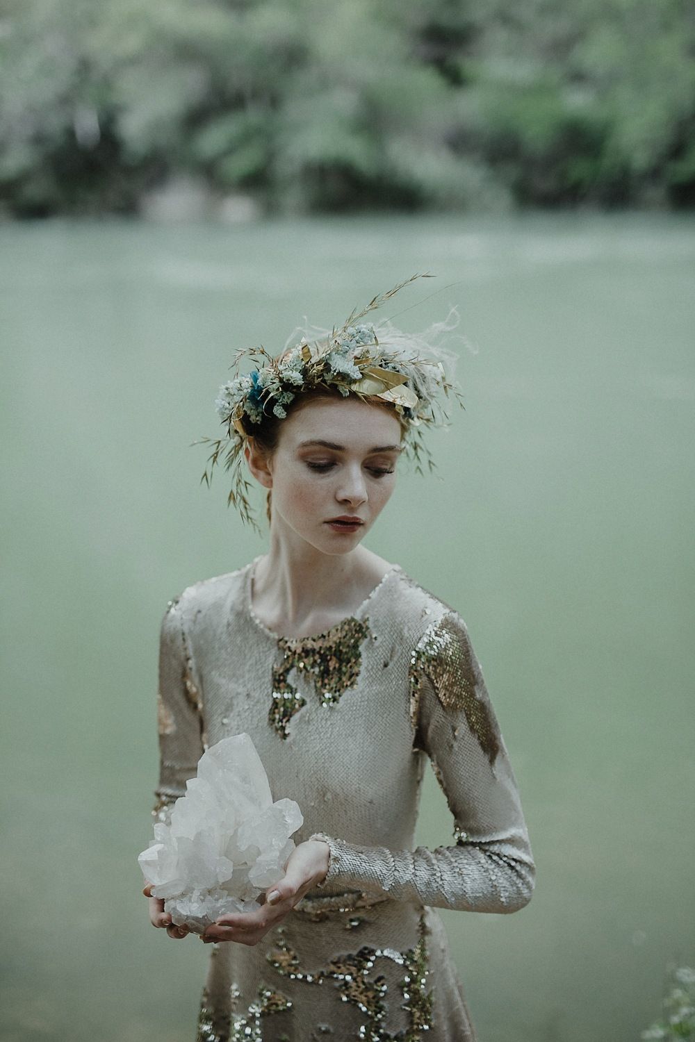 Ethereal figure in a sparkly dress and floral crown holds crystals in a misty forest setting.