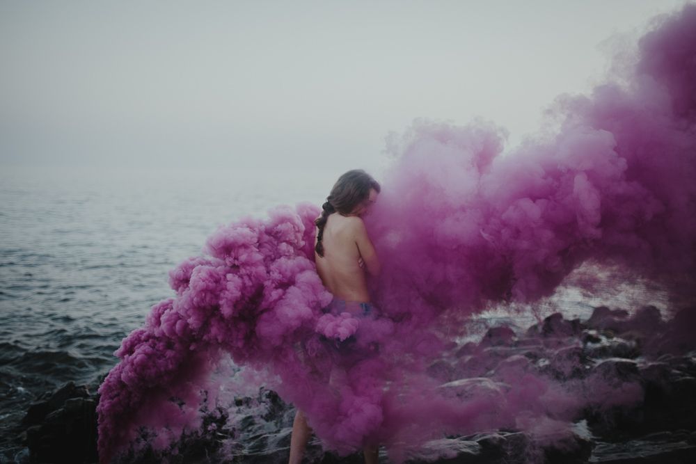Artistic portrait with vibrant purple smoke bombs creates dramatic effect against ocean backdrop.