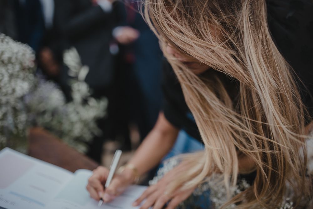 Close-up of someone signing the wedding register with white flowers in the background.