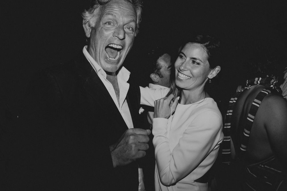 Two people share a joyful candid moment at a party, captured in black and white.