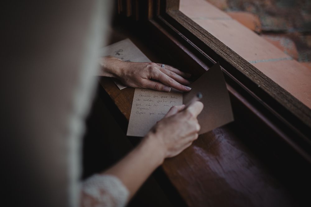 Hands writing on paper by window light, capturing intimate wedding day moment.