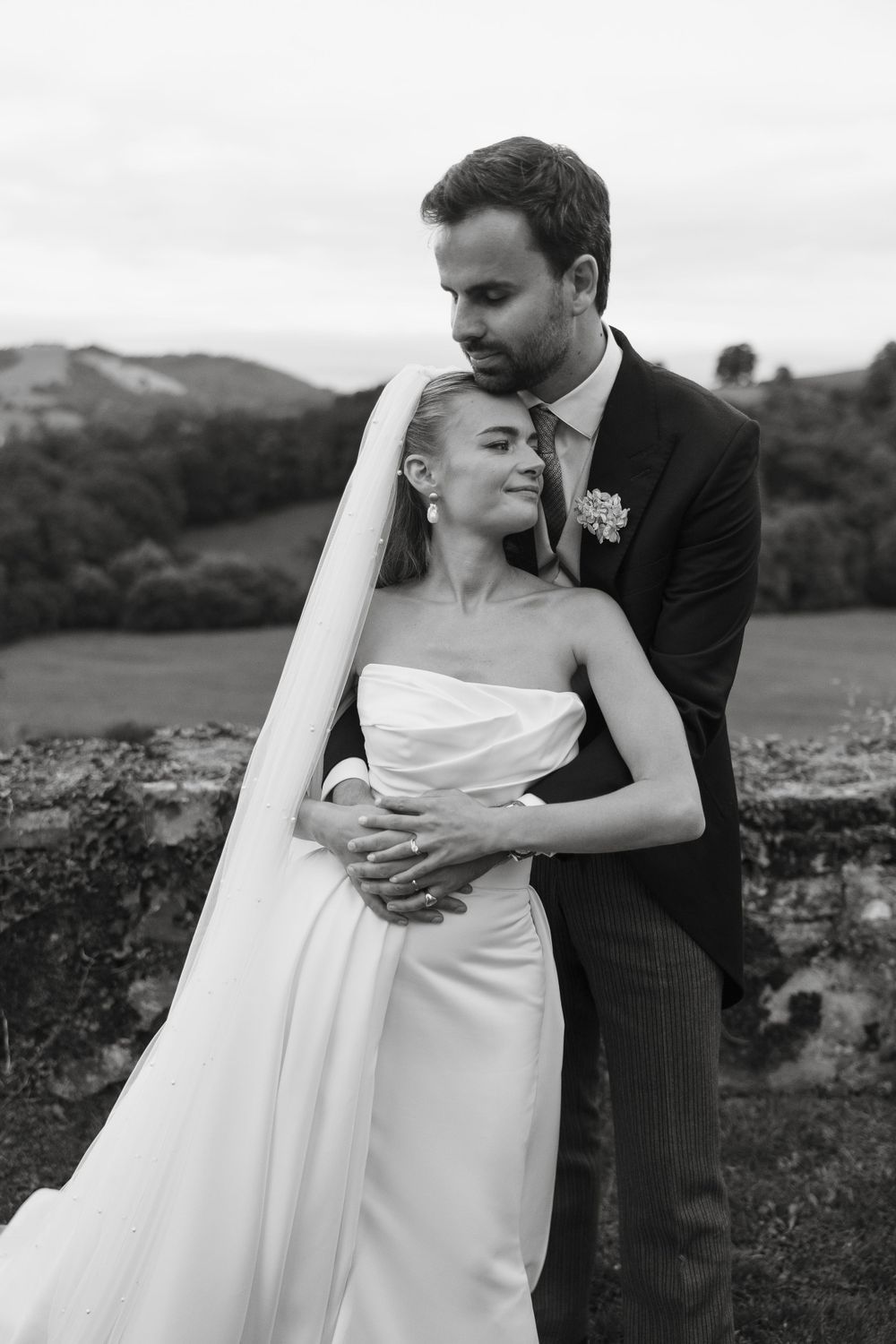 Elegant couple shares an intimate moment in their wedding attire against a mountainous landscape.