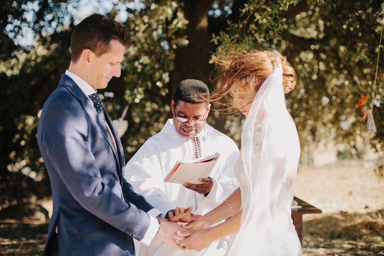 A wedding ceremony moment captured under a tree with an officiant reading from a book.