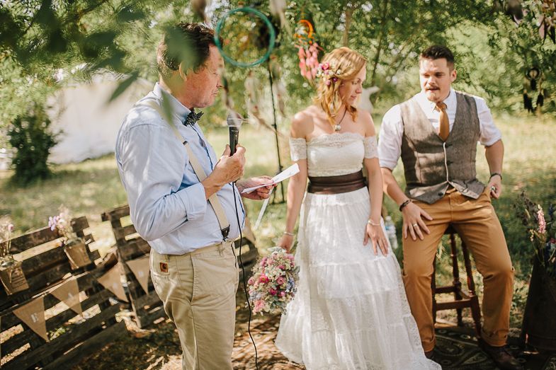 An outdoor wedding ceremony takes place in a sunny garden setting with rustic decor.