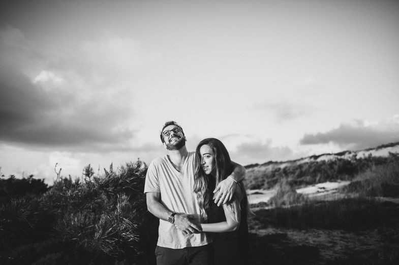 A couple stands together in black and white photography against a hillside landscape.