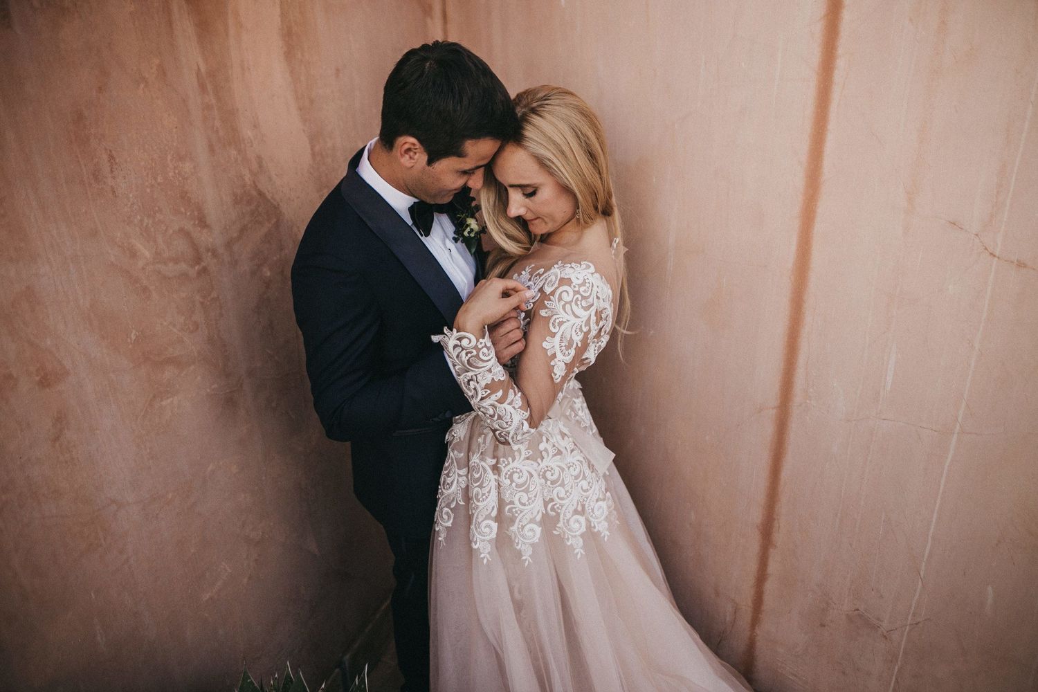 Intimate wedding portrait of couple in formal attire against pink wall.