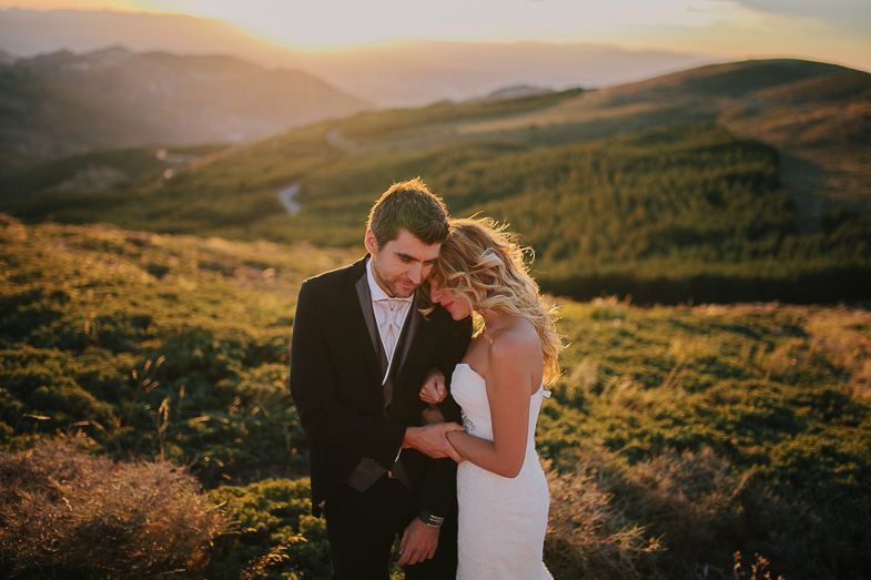 A couple shares an intimate moment at sunset on a mountaintop in formal wedding attire.