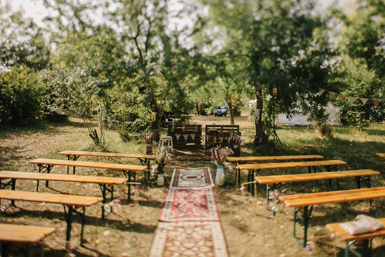 Outdoor wedding ceremony setup with wooden benches arranged in rows among trees.