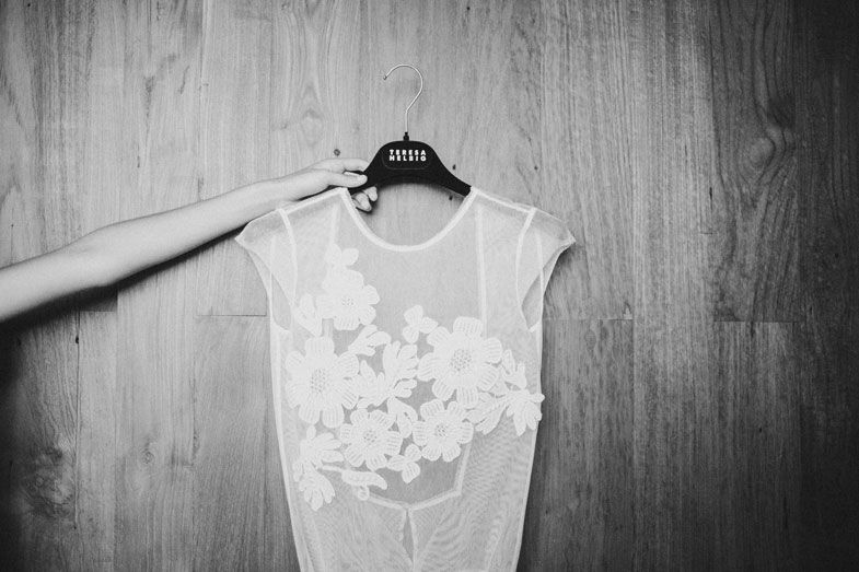 White lace sleeveless dress hanging against wooden wall background.