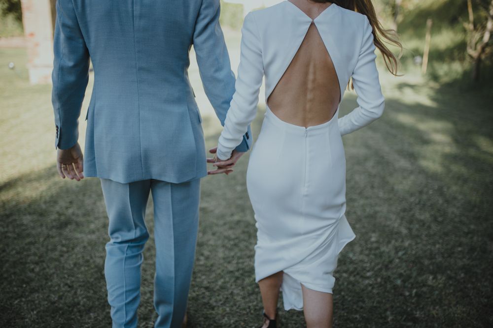 Back view of couple holding hands showing elegant blue suit and white dress with keyhole detail.