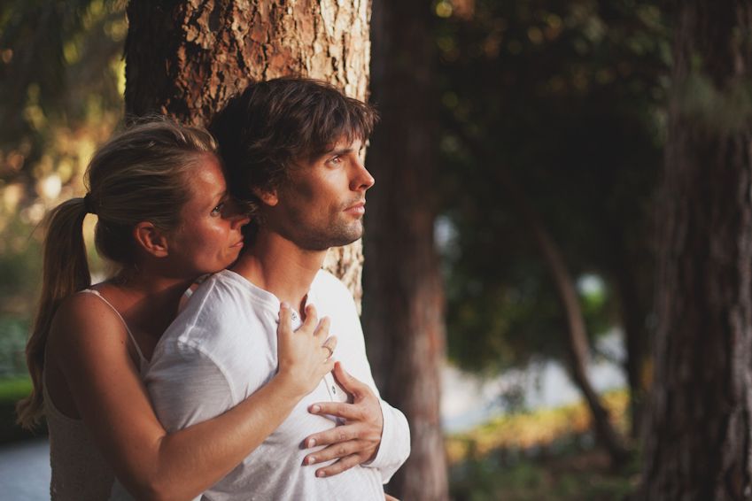 Couple embracing tenderly among pine trees in natural outdoor setting.
