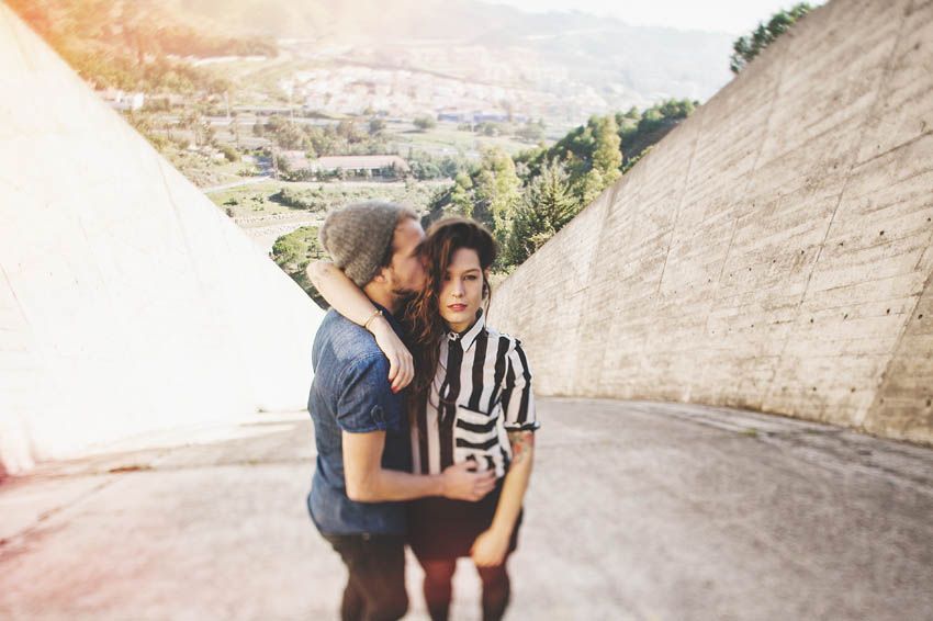 Two people share a playful moment against concrete walls with mountains in the background.