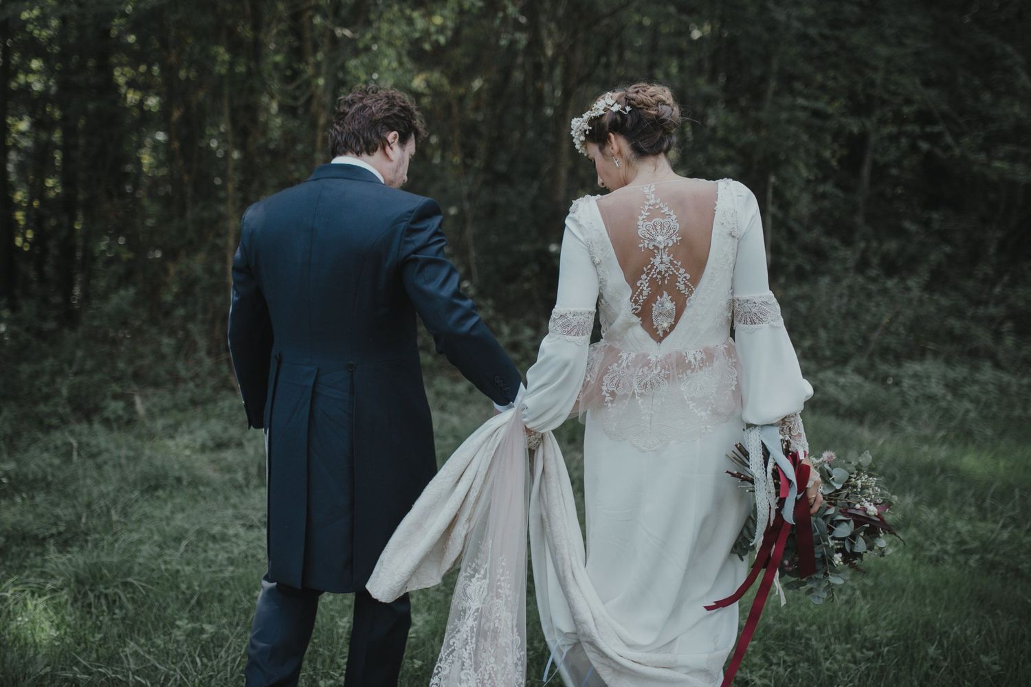 Romantic wedding couple walking through forest clearing in vintage-inspired attire.