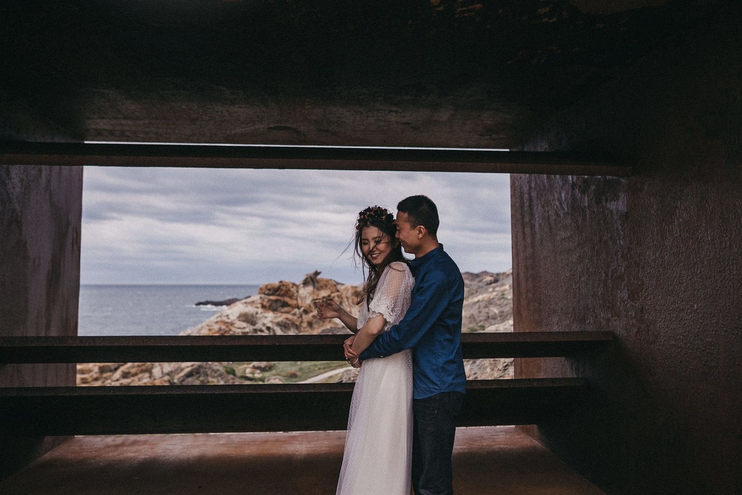 A romantic moment captured through a concrete frame with rocky coastline in the background.