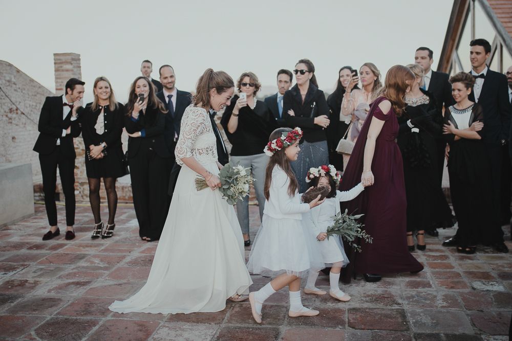 Wedding party in formal attire gathering on stone courtyard during ceremony.