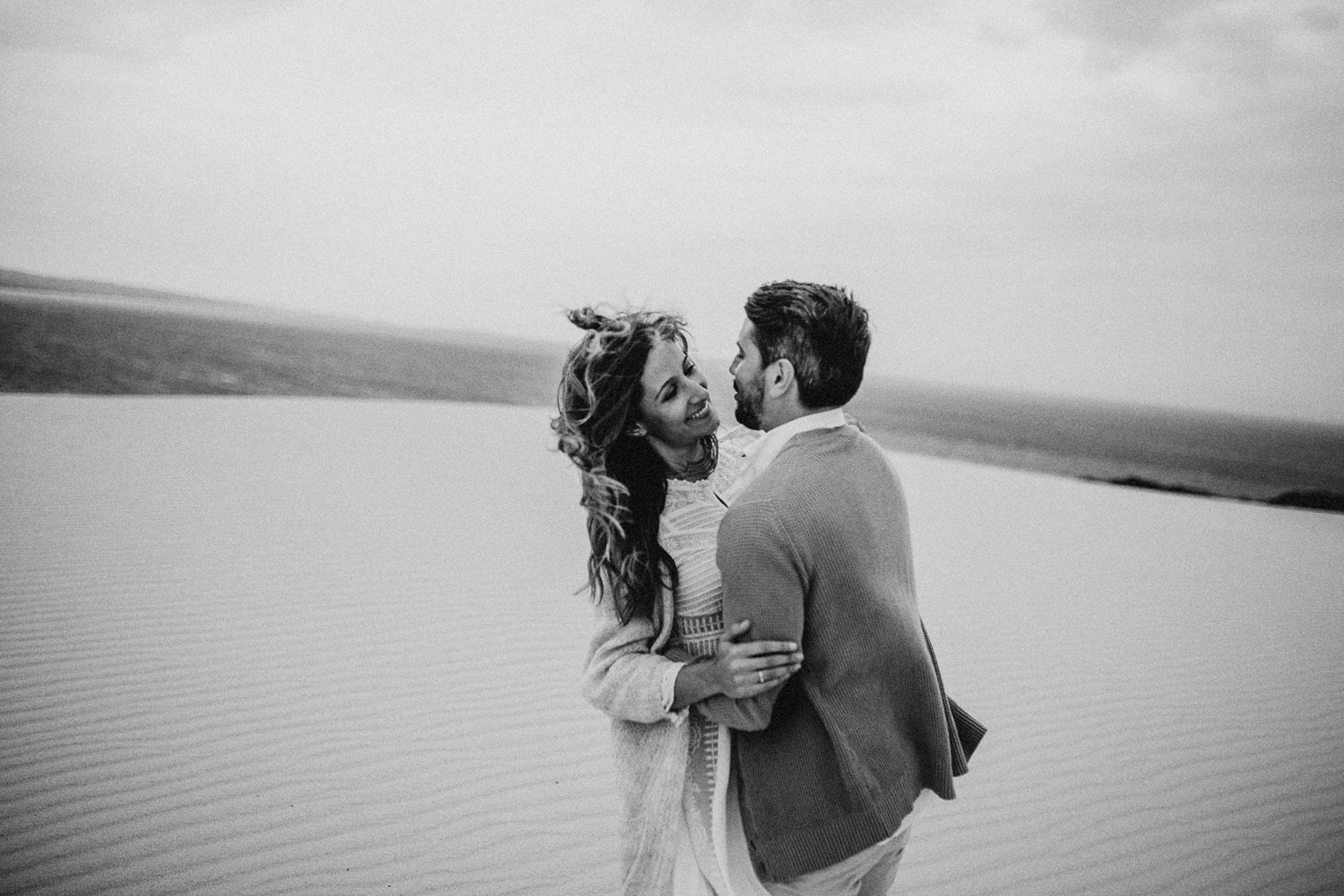 Romantic couple embracing on sand dunes with dramatic cloudy sky background.