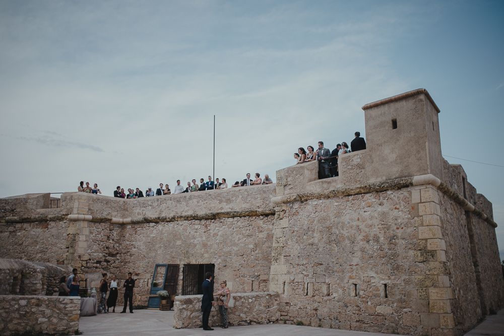 Ancient stone fortress walls with people gathered on top against blue sky.