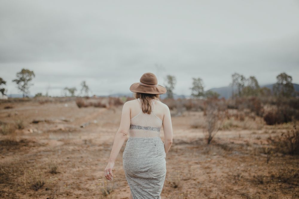 Figure in a hat and dress walks through desert landscape on cloudy day.