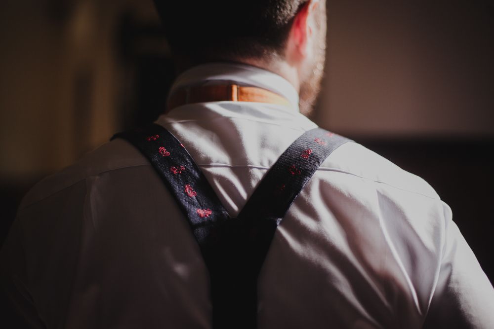 Back view of person wearing white dress shirt and suspenders in dark room.