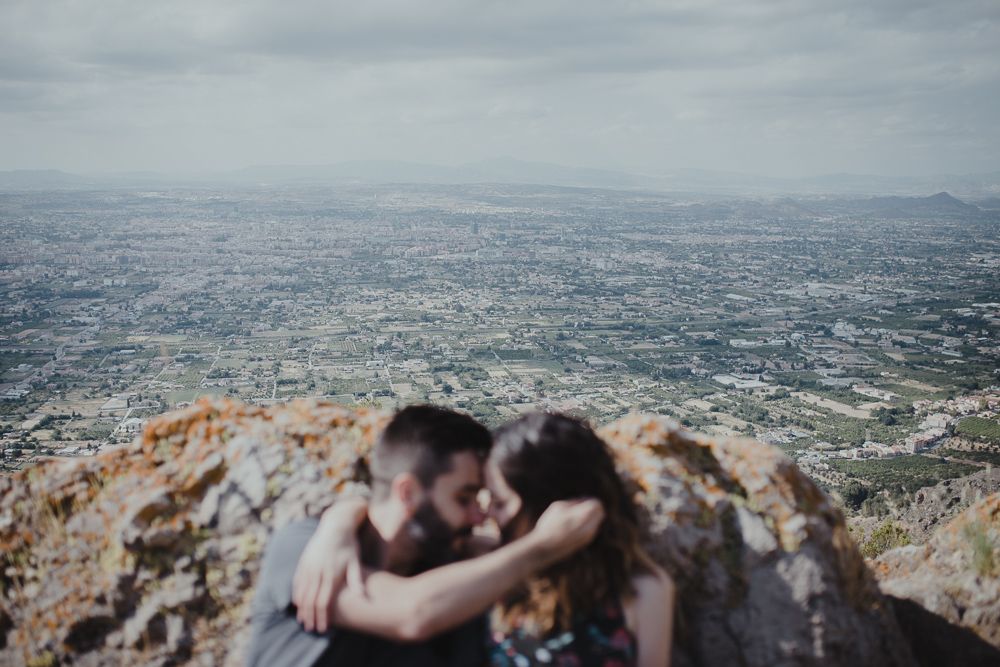 Couple sharing an intimate moment on a mountain overlook with cityscape vista below.