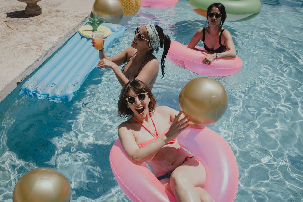Pool party scene with pink floaties and gold balloons in blue water.