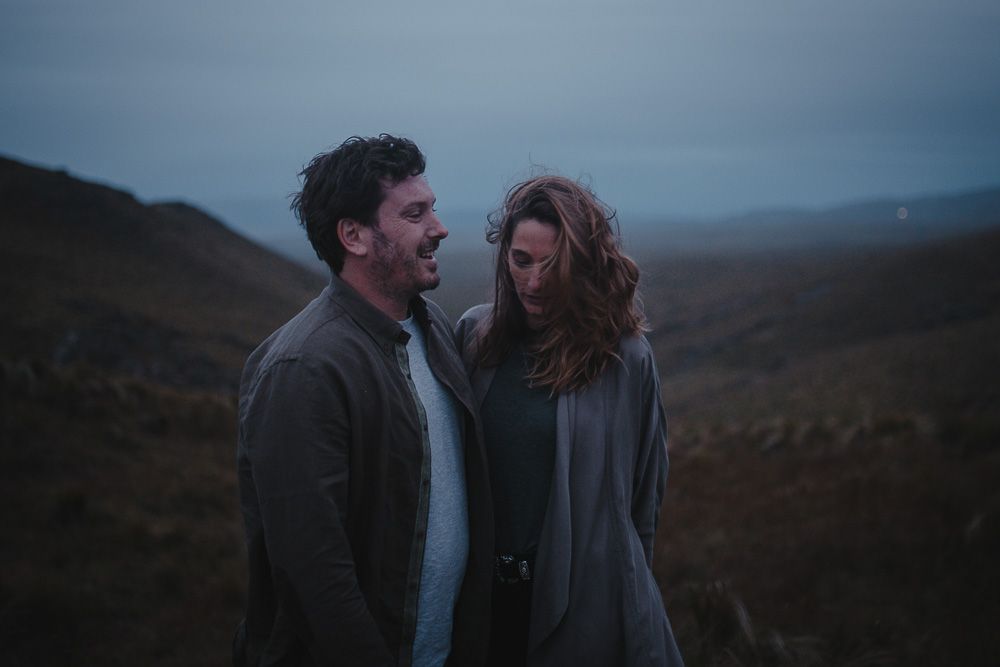 Two people embrace closely in dramatic mountain setting during overcast evening.