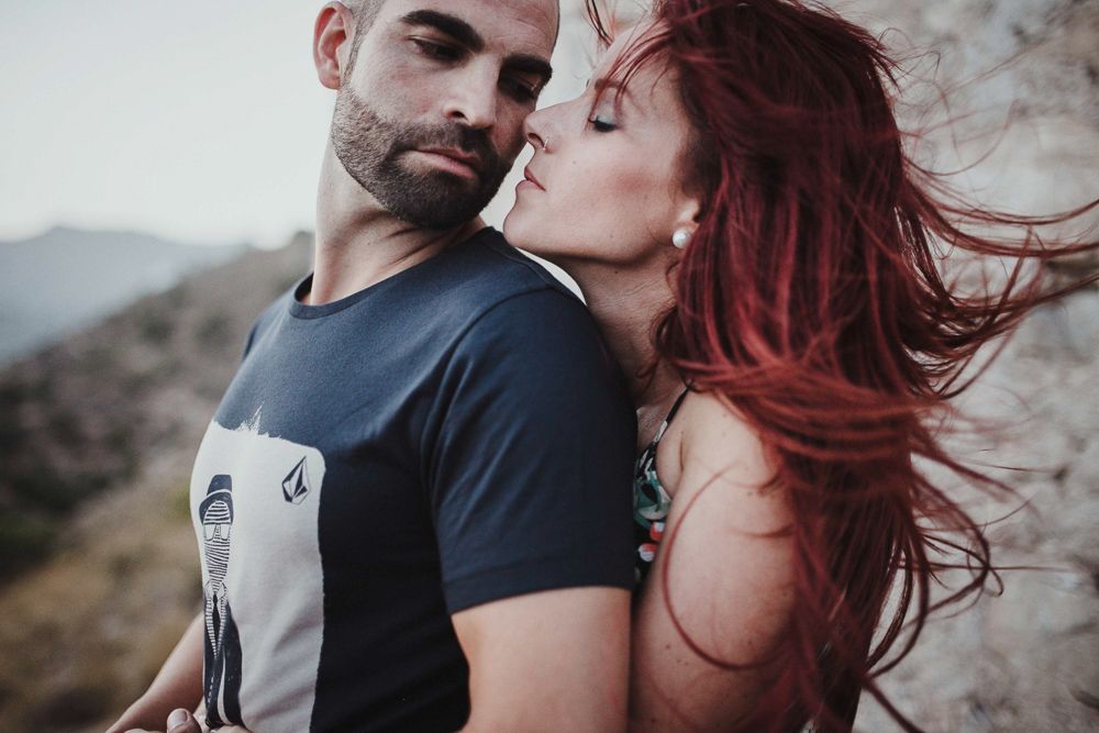 Artistic portrait of couple with vibrant red hair against mountain backdrop.