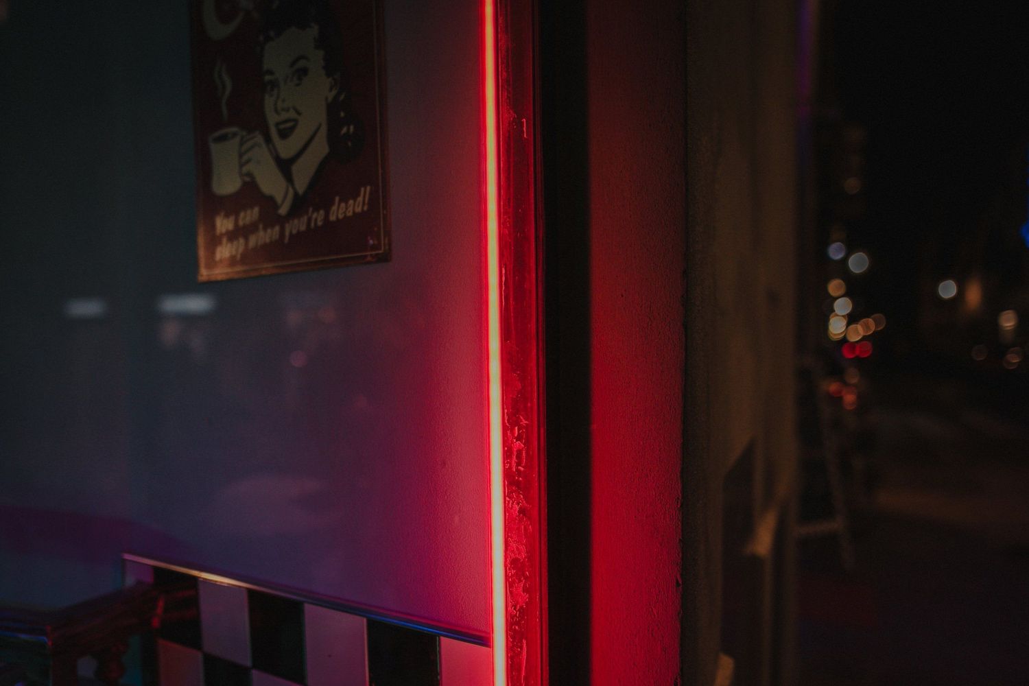 Red neon light illuminating a dark urban street corner at night.