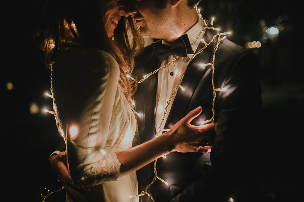 Couple dances together surrounded by twinkling lights in an artistic moody shot.