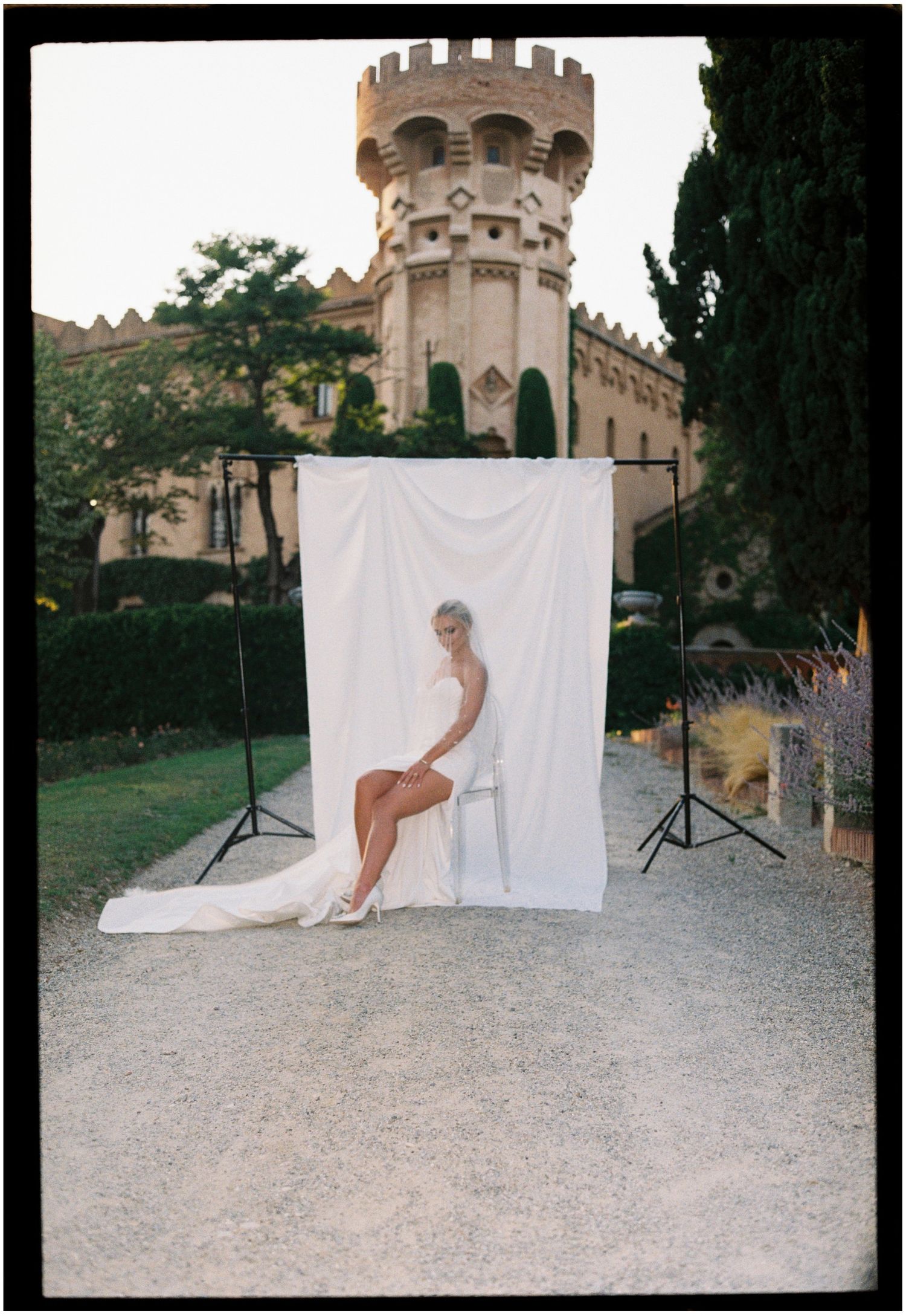 Wedding photo setup with white backdrop and castle tower visible in European garden setting.