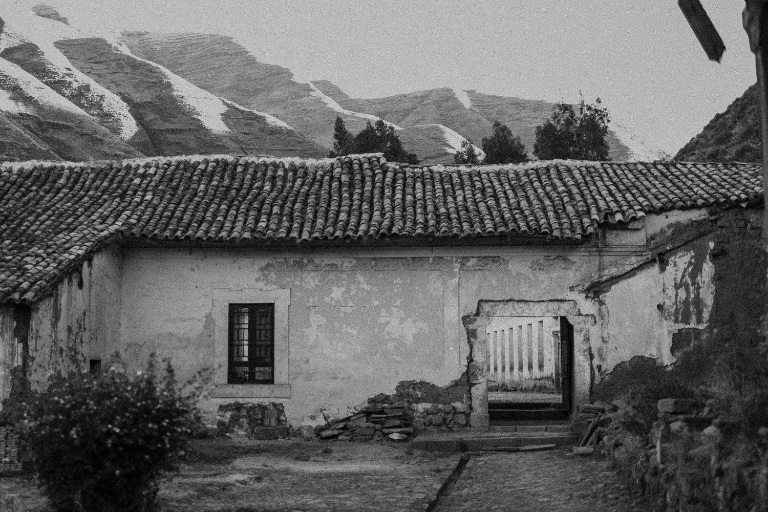 A rustic stone house with tiled roof and mountain backdrop in black and white.