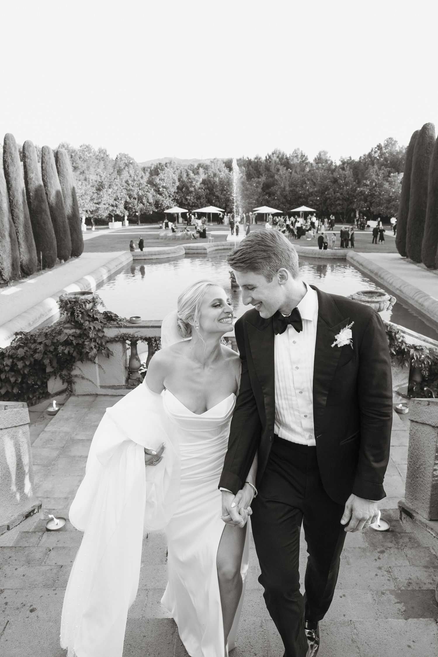 Bride and groom sharing intimate moment by fountain with cypress trees in background.