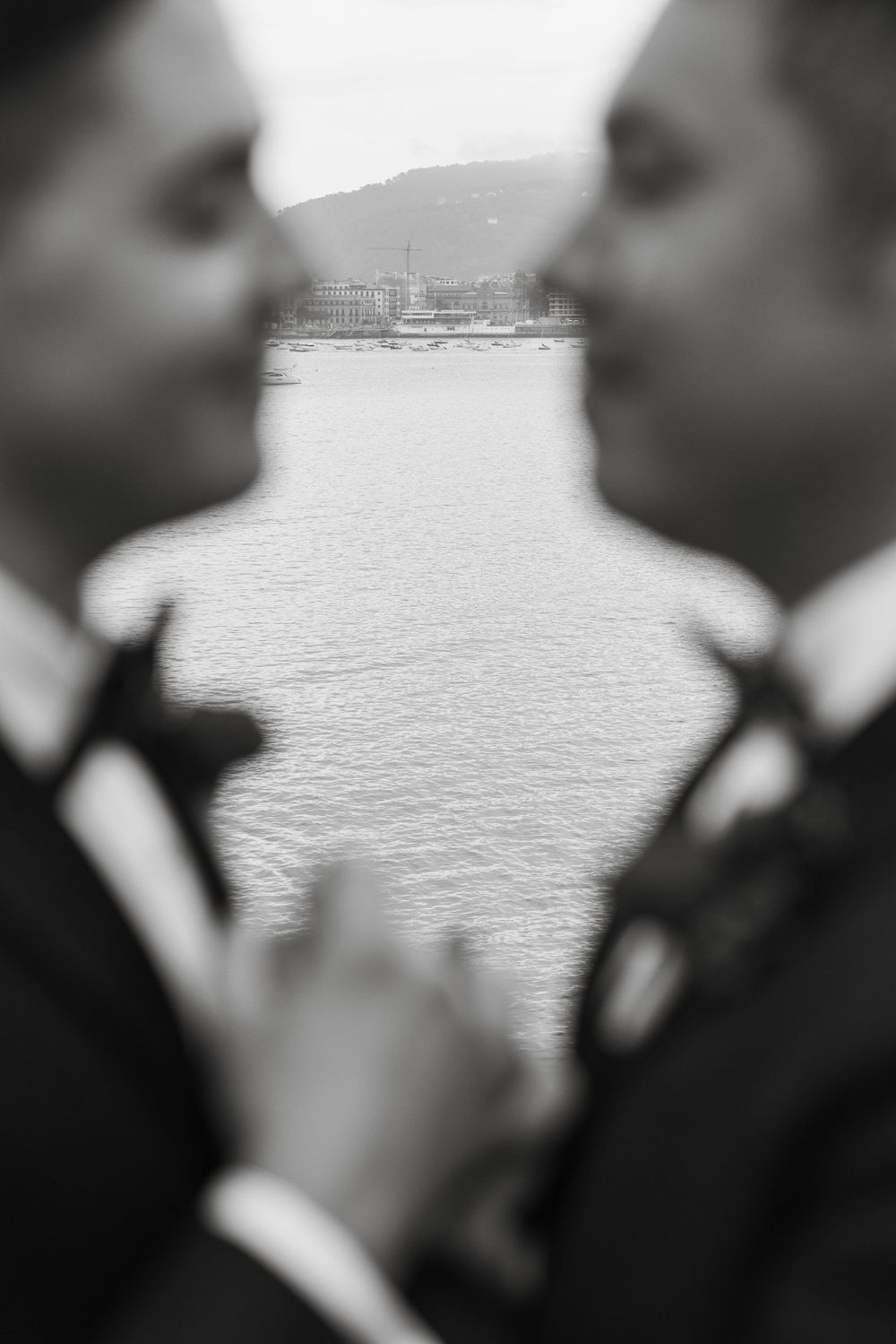 Artistic black and white wedding portrait with water and cityscape in background.