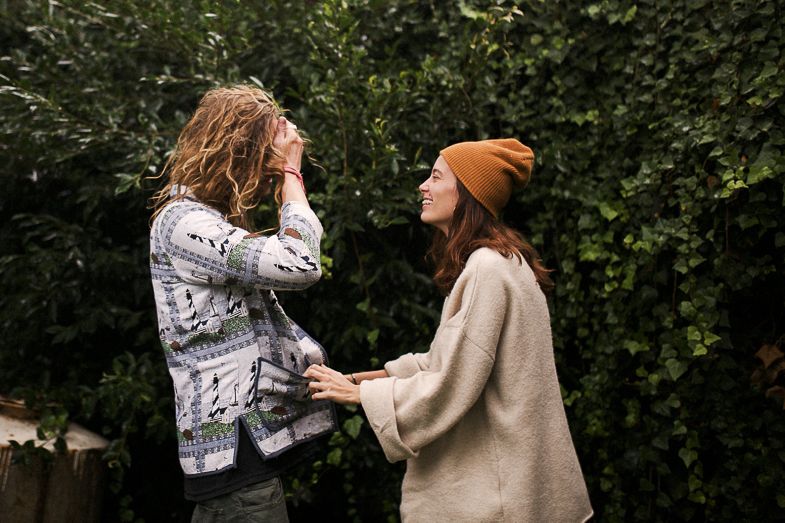 Two people holding hands and smiling in front of a leafy garden backdrop.