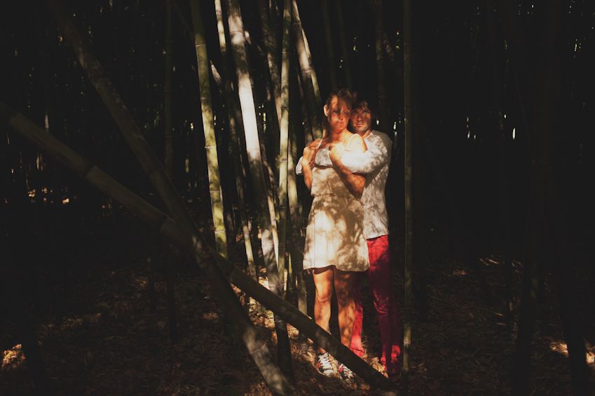 Couple sharing intimate moment between trees with dramatic lighting.