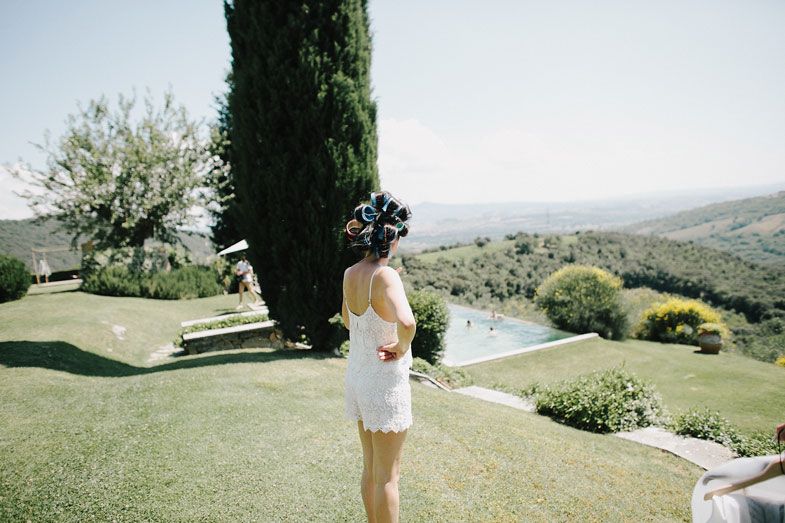 Figure in white dress standing against backdrop of Tuscan hills and cypress trees.