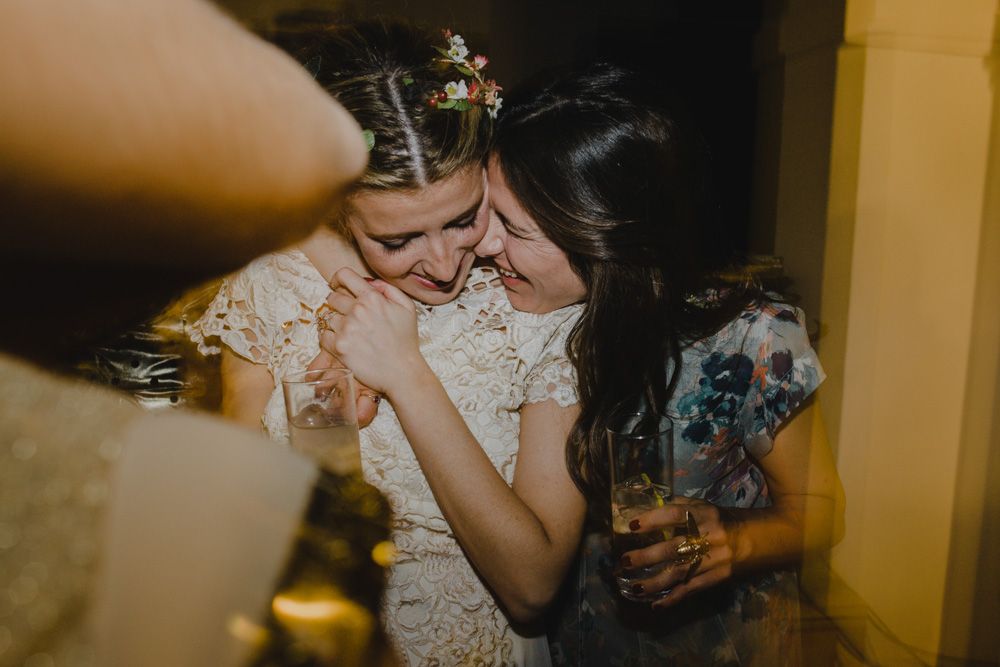Someone in a delicate white lace wedding dress laughs while holding a drink at a celebration.