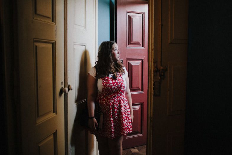 Figure standing in doorway between rooms with red door frame and dark dramatic lighting.