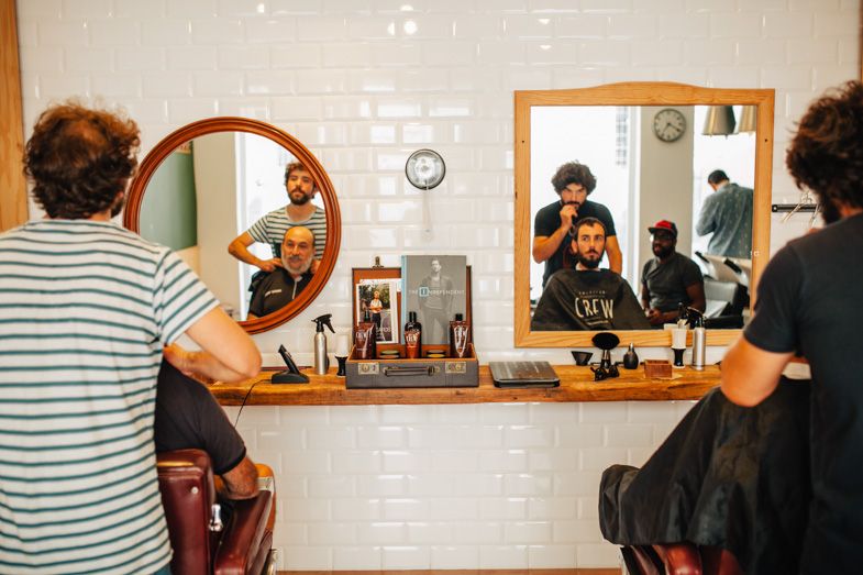Interior of a barbershop with white subway tile walls and circular mirrors at styling stations.