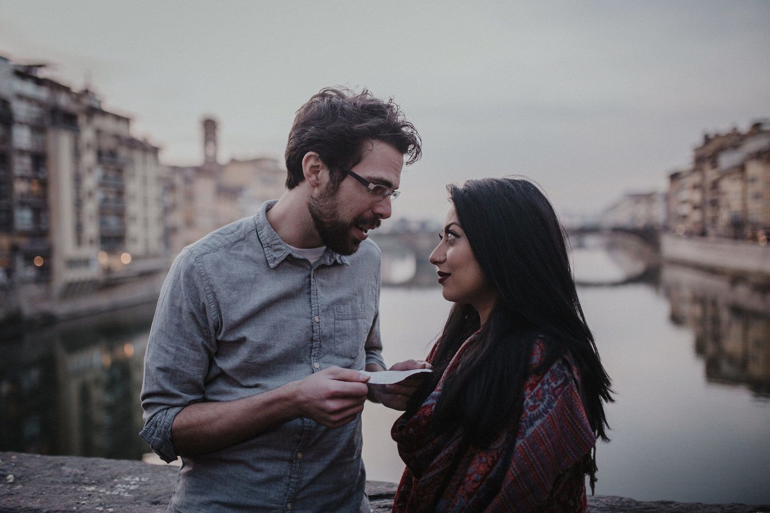 A couple having an intimate conversation on a bridge overlooking an Italian canal.