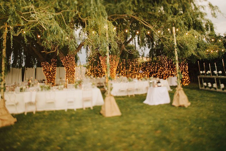 Outdoor wedding reception setup with string lights hanging between trees.