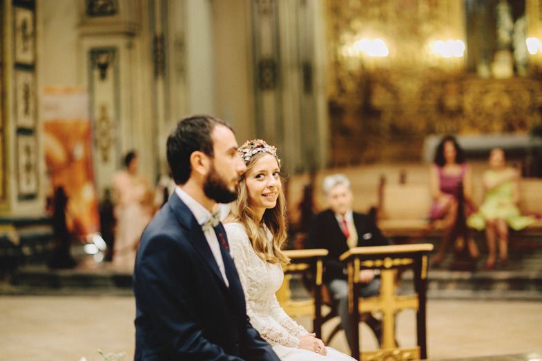 A couple sits together in a beautifully lit historic church during their wedding ceremony.