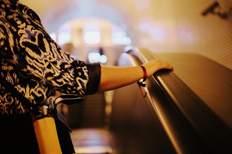 Hand in patterned sleeve gripping a metal railing in dim lighting.
