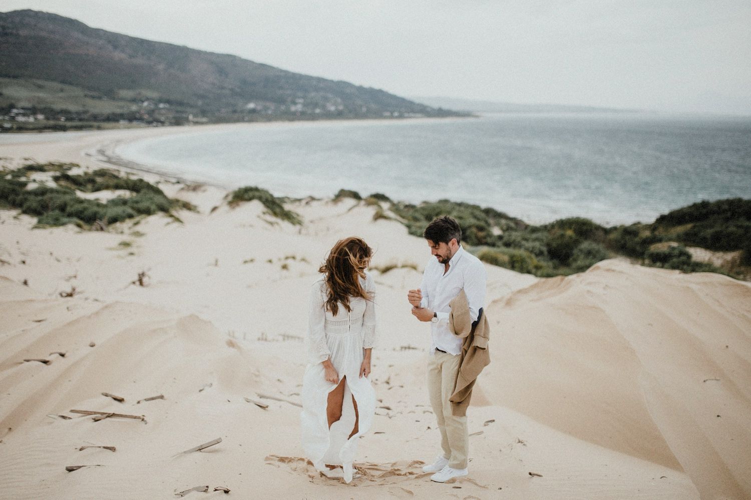 A couple walking hand in hand on sandy dunes by the ocean coastline.