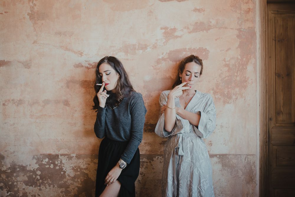 Two people leaning against weathered pink wall in contrasting outfits.