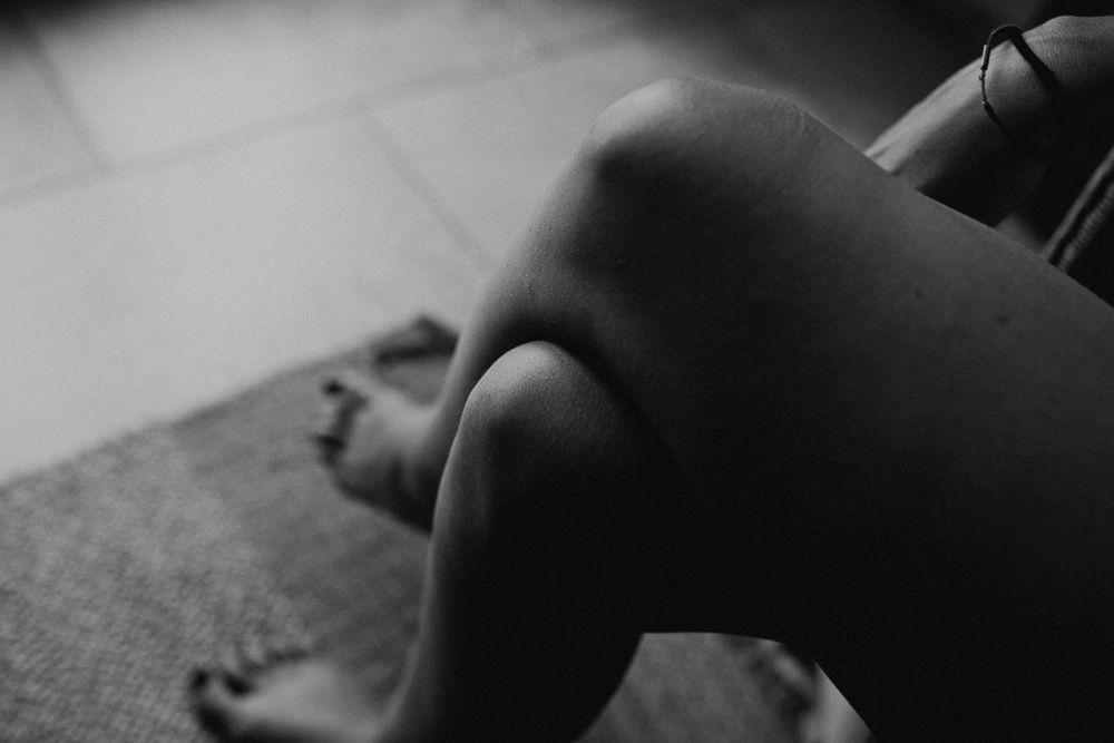 Artistic black and white photograph of bare legs resting on textured surface.