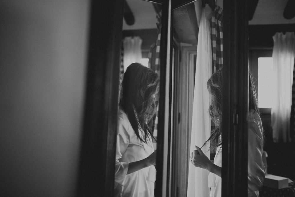 A person in white robe standing beside a mirror in moody black and white lighting.